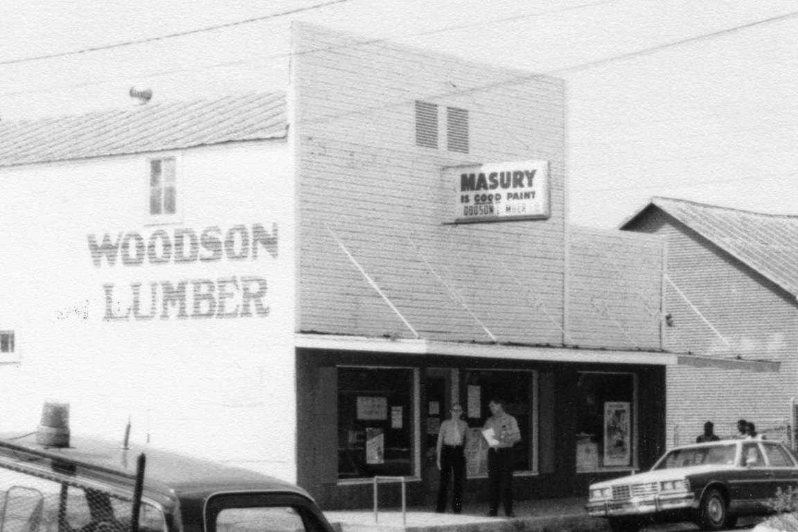 A historic black-and-white photo of the Woodson Lumber storefront with a Masury paint sign