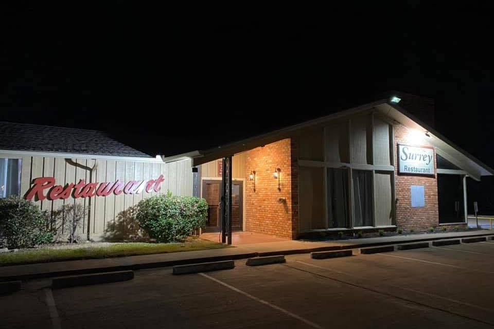 The Surrey Inn restaurant building at night, with a red Restaurant sign on the left wall, a brick entry and a lit Surrey Restaurant sign.