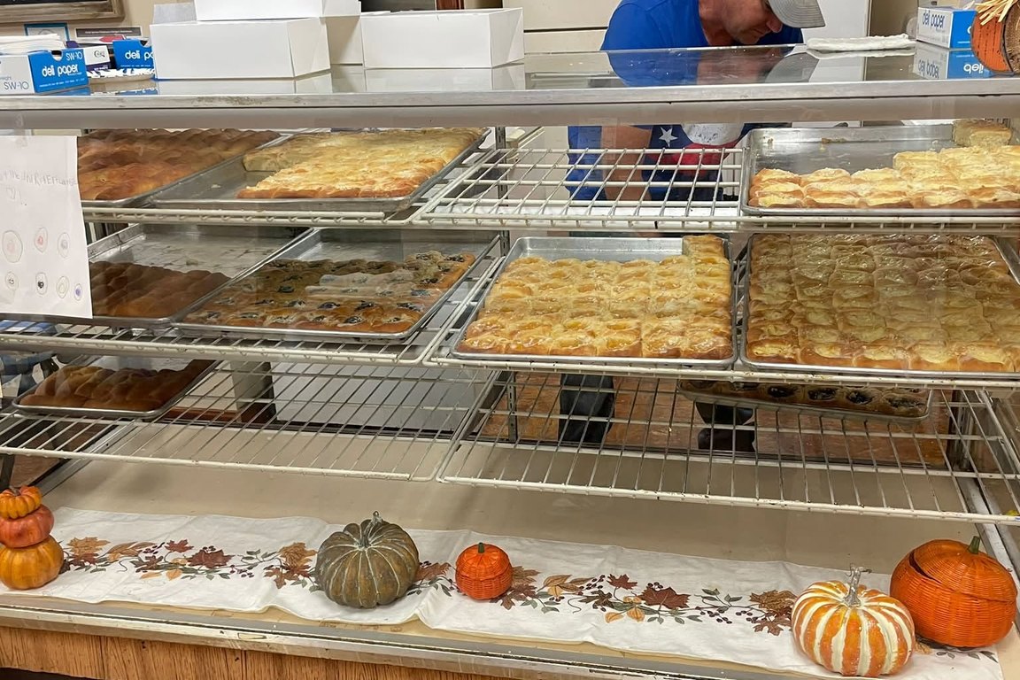 A bakery display case holding trays of kolaches and pastries, with small pumpkins on the counter.
