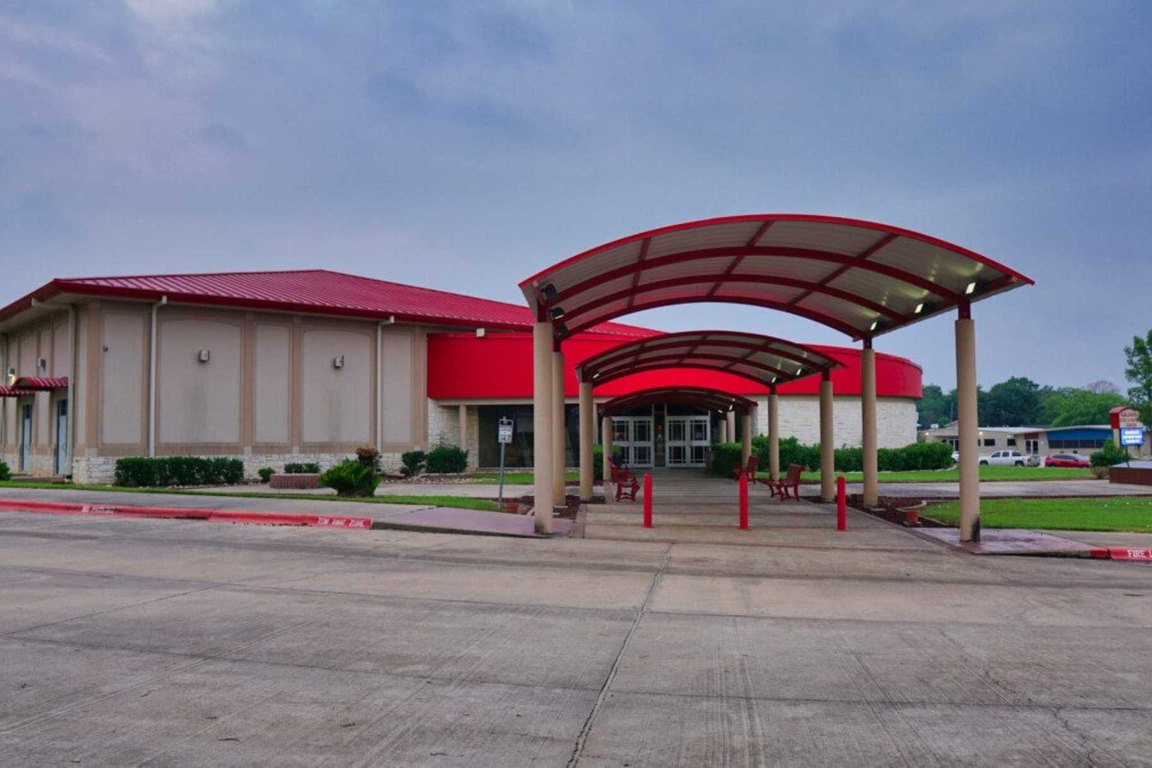 A tan one-story civic center with a red roof and a curved red canopy over the entrance walkway.