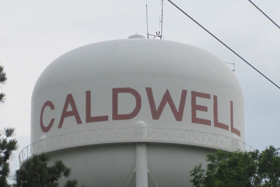 A white water tower tank painted with the word CALDWELL in red letters.