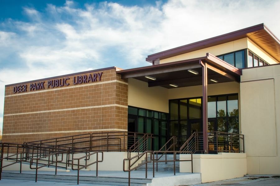 A modern brick and glass building with a sign reading Deer Park Public Library and railed entrance ramps.