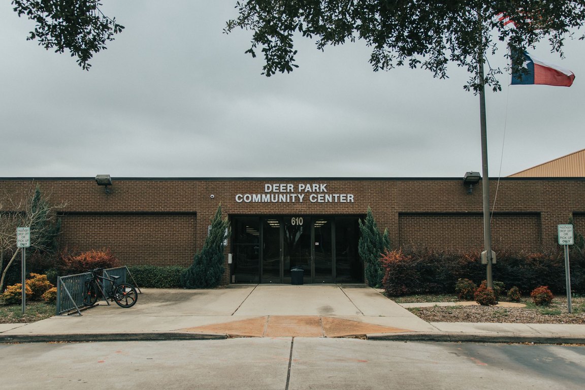A low brick building with a sign reading Deer Park Community Center, with a Texas flag on a pole beside it.