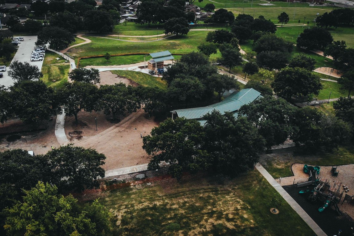 An aerial view of a wooded park with walking paths, a pavilion roof and a playground.