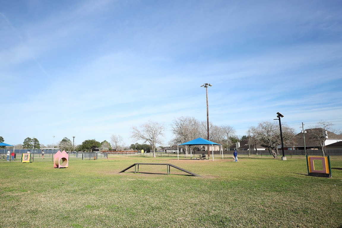 The fenced dog park at Independence Park with agility equipment on the grass.