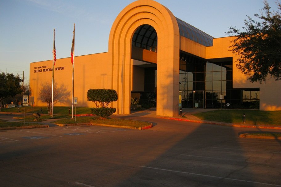 The George Memorial Library building, with a large arched entrance and flags out front, lit by evening sun.
