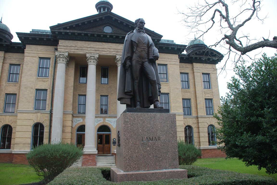 A bronze statue of Mirabeau B. Lamar on a granite base in front of the columned Fort Bend County Courthouse.