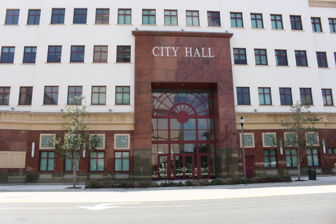 The red-stone main entrance of West Palm Beach City Hall with the words City Hall above the doors.