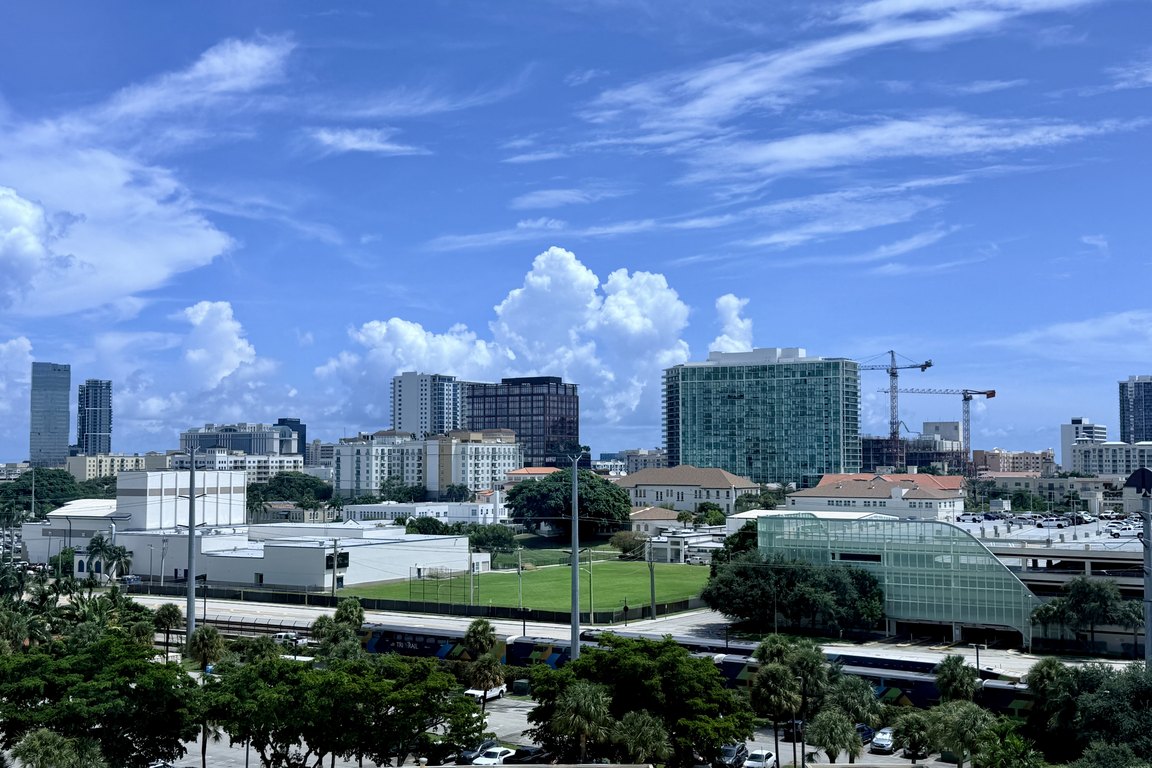 A daytime view over low buildings and trees toward the downtown West Palm Beach skyline under a blue sky.