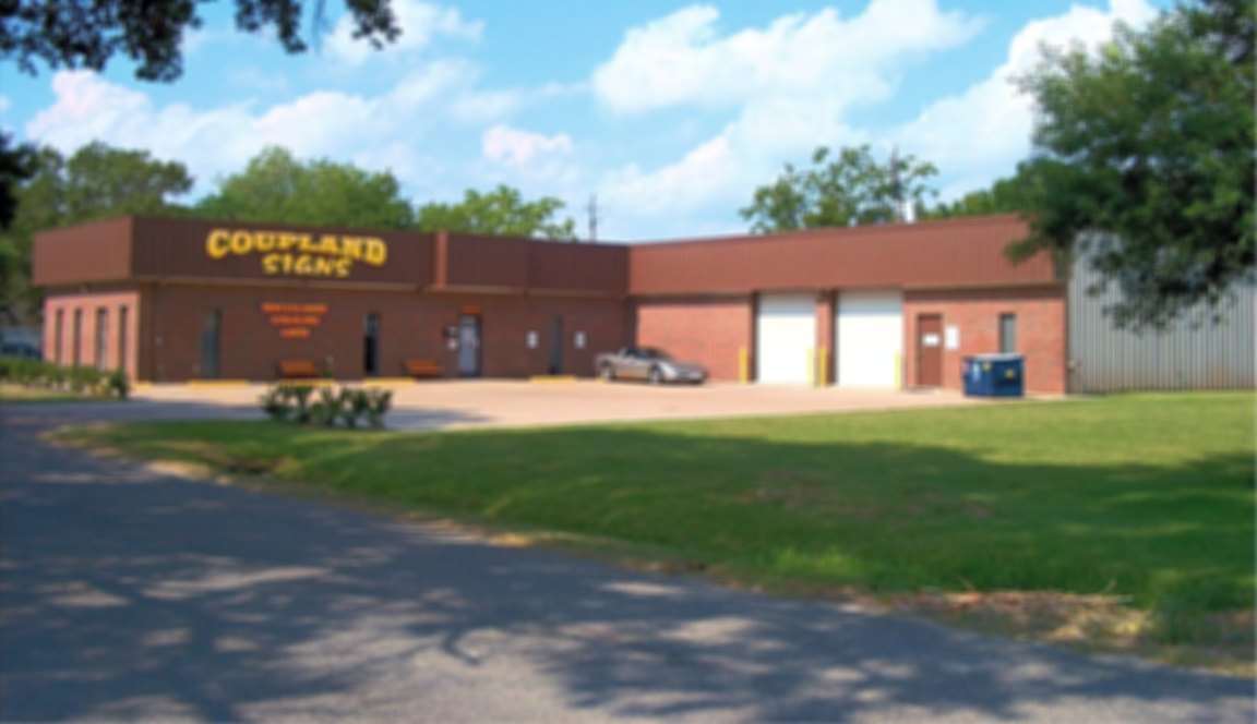 Coupland Signs' red-brick shop with yellow lettering and two white roll-up doors