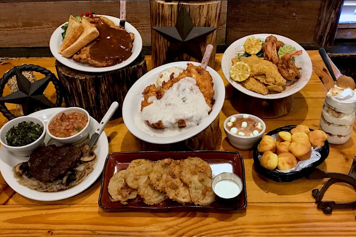 A table of plates at The Southern Komfort Kitchen: a gravy-covered country-fried entree, a fried seafood platter, fried green tomatoes, cornbread muffins and a dessert in a jar.