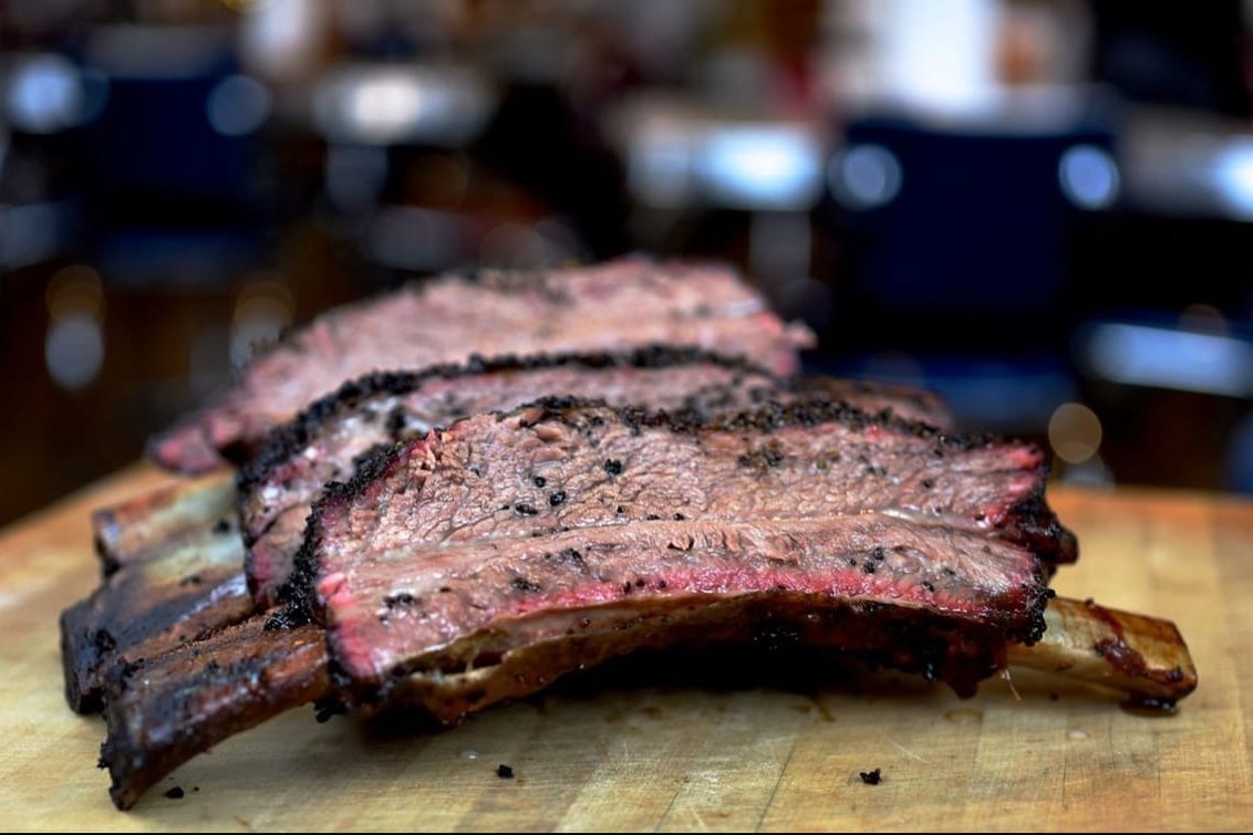 Thick slices of a smoked beef rib with a peppered bark on a wooden cutting board