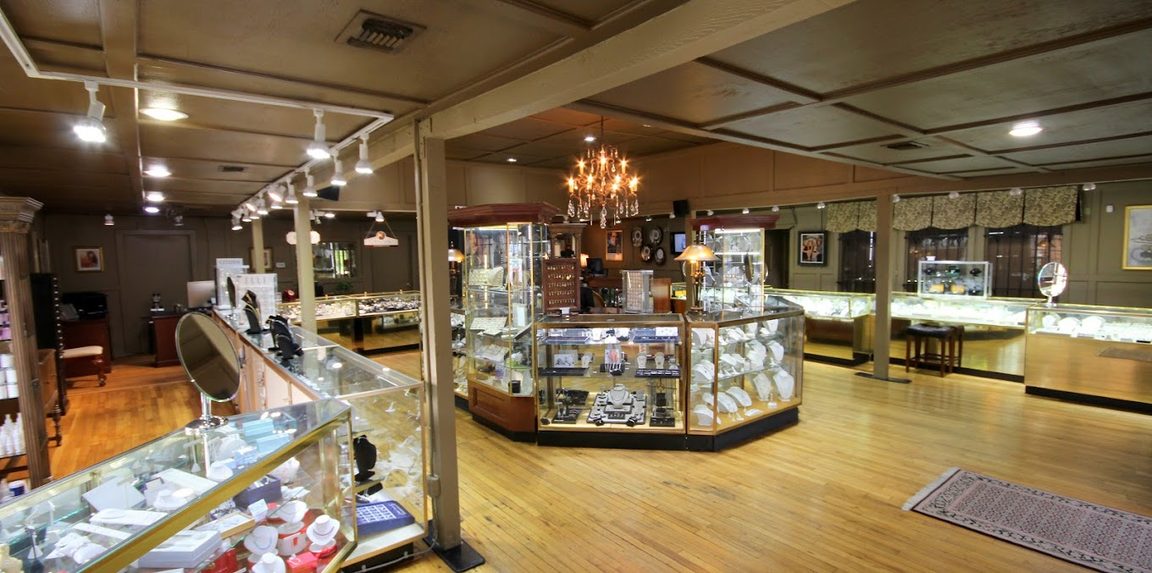 Glass display cases under a chandelier in the Gold Connection Jewelers showroom