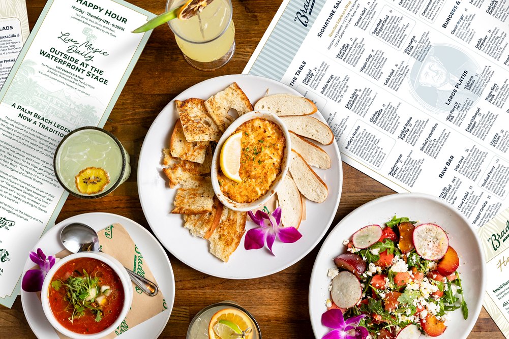Crab dip, soup, a salad and cocktails laid out on E.R. Bradley's printed menu