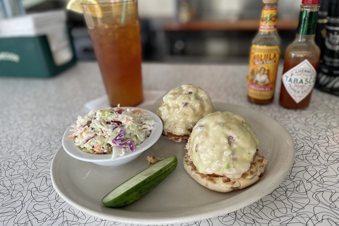 A plate at Howley&rsquo;s with two cheese-topped sandwich halves, coleslaw and a pickle spear beside an iced tea on a boomerang-pattern counter